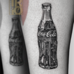 Tatuaggio Coca Cola black and grey sulla gamba con bottiglietta iconica in stile illustrativo e dettagli vintage