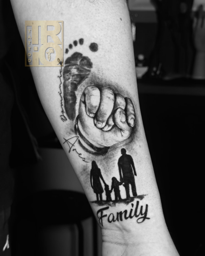 tatuaggio realistico black and grey sull’avambraccio con impronta di neonato, mano di bambino, silhouette di famiglia e scritta Family